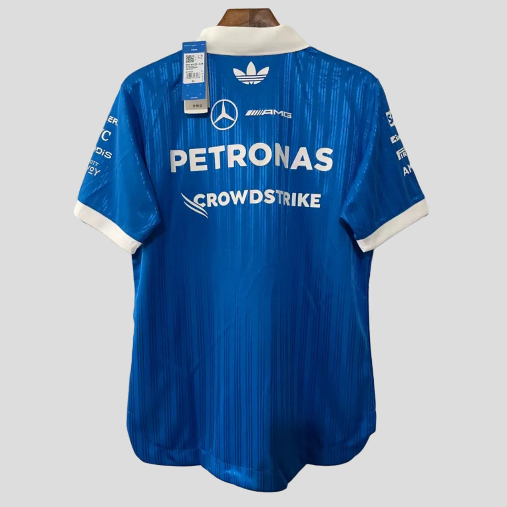 A blue Adidas Mercedes Petronas Crowdstrike cycling jersey shown from the back, hanging on a wooden hanger against a white brick wall. The jersey features white sponsor logos and the Mercedes star logo.