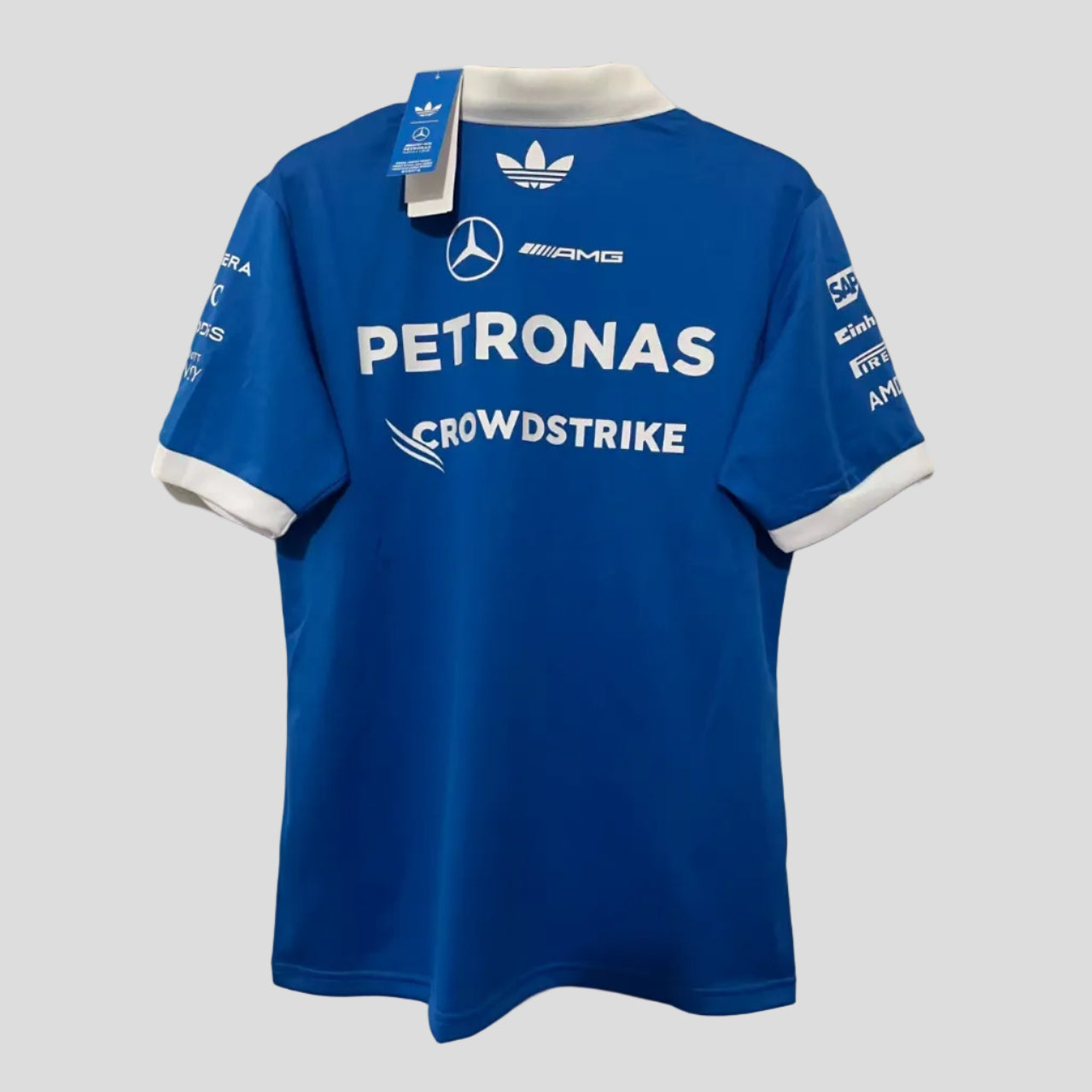 A blue Mercedes-AMG Petronas Crowdstrike short-sleeve jersey by Adidas, shown from the back hanging on a wooden hanger against a white brick wall. The jersey features white sponsor logos and the Adidas trefoil logo.