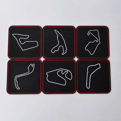 Six black square coasters with rounded corners arranged in a 2x3 grid on a light gray background. Each coaster features a white outline of a Formula 1 track circuit and has a thin red border.
